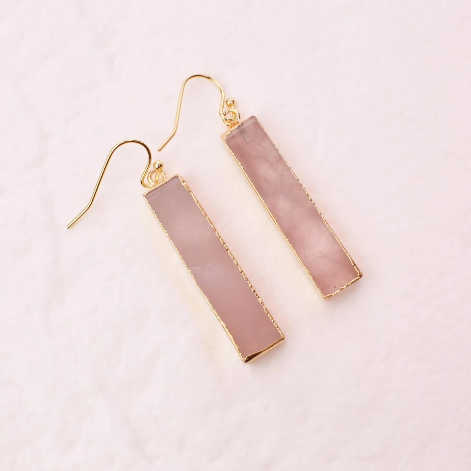 Faceted rectangle rose quartz drop earrings on a neutral display cup.