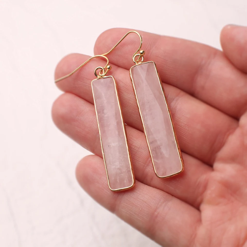 Faceted rectangle rose quartz drop earrings on a neutral display cup.