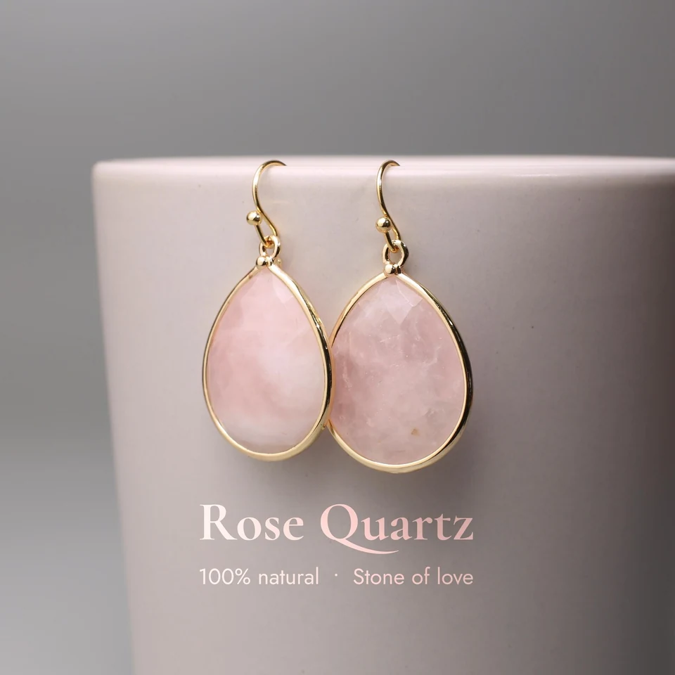 Faceted teardrop-like rose quartz drop earrings on a neutral display cup.